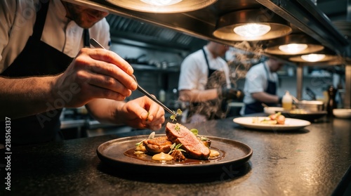 Close up of professional chef plating gourmet meat dish under warm lights in high end restaurant kitchen