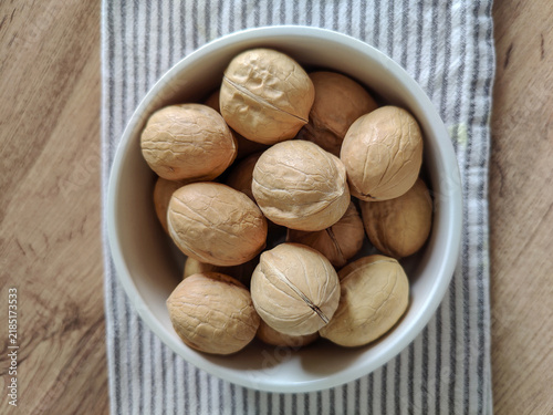 Whole walnuts in white ceramic bowl and striped kitchen cotton towel on wooden table.  Healthy eating, calories, diet, harvest. Shells of washed nuts are perfectly clean. Copy space. Close-up.