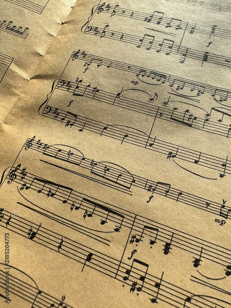 Fototapeta premium Close up of old sheet music with musical notes and clefs. Old musical score - no lyrics. Atmospheric music background with notes on old brown paper. Image of a sheet of music with notes. Scrapbooking