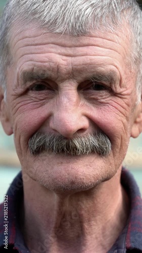 Close-up portrait of an elderly man with a gray mustache looking at the camera. Authentic wrinkled face, kind expression, senior outdoors.