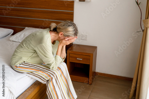 Quadro su tela Middle aged woman sits on bed covering face with hands in distress