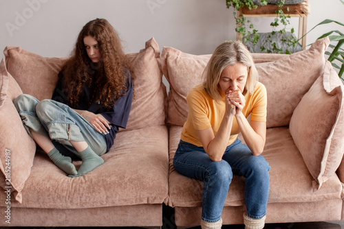 Konstfotografi Middle aged woman leans forward with troubled expression while teenage girl sits apart and avoids eye contact, showing family tension