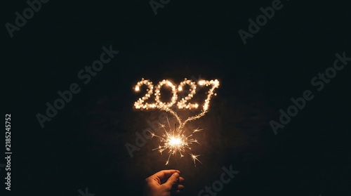 Sparkling 2027 New Year number written with sparkler light. Glowing 2027 firework digits on black background. Festive holiday celebration.