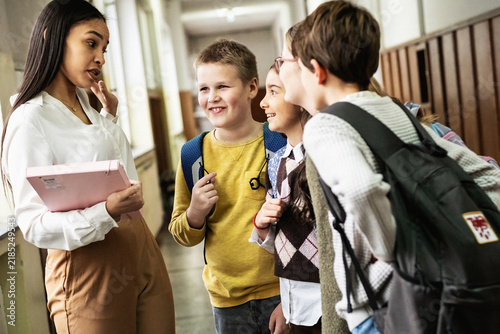 The teacher walks through the school lobby while speaking with her students as class is about to begin. The moment feels relaxed and friendly, with everyone easing into the school day.