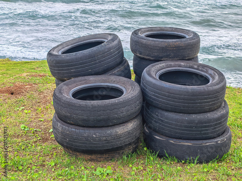 Фотография Stack of old used rubber tires piled up on a grassy coastal shore near the sea with ocean waves in the background