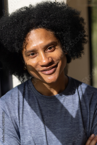 Adult African American man smiling and tilting head, wearing grey tee, showing nose hoop