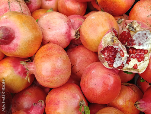 Display of ripe pomegranates with one fruit split open to reveal juicy red seeds, fresh seasonal fruit for sale.