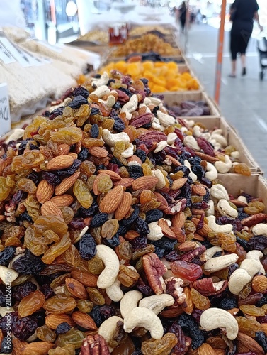 Market stall display with assorted bulk nuts for sale by weight, including walnuts, cashews, almonds, and mixed nuts.