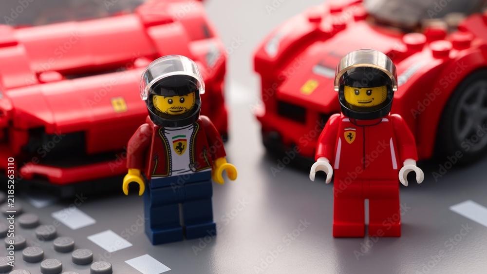 Fototapeta premium Tambov, Russian Federation - July 12, 2026 Lego Ferrari racing driver minifigures standing on a road plate with red Ferrari sports cars in the background. Lego Speed Champions.