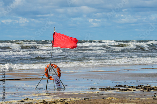 Принти на полотні Red Warning Flag and Lifebuoy on Stormy Baltic Sea Beach with Rough Waves and St