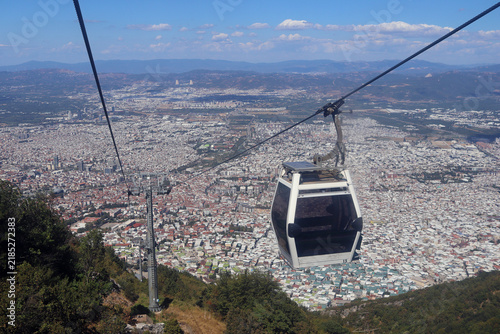 Quadro su tela Aerial view of a white cable car cabin gliding over a vast cityscape with endles