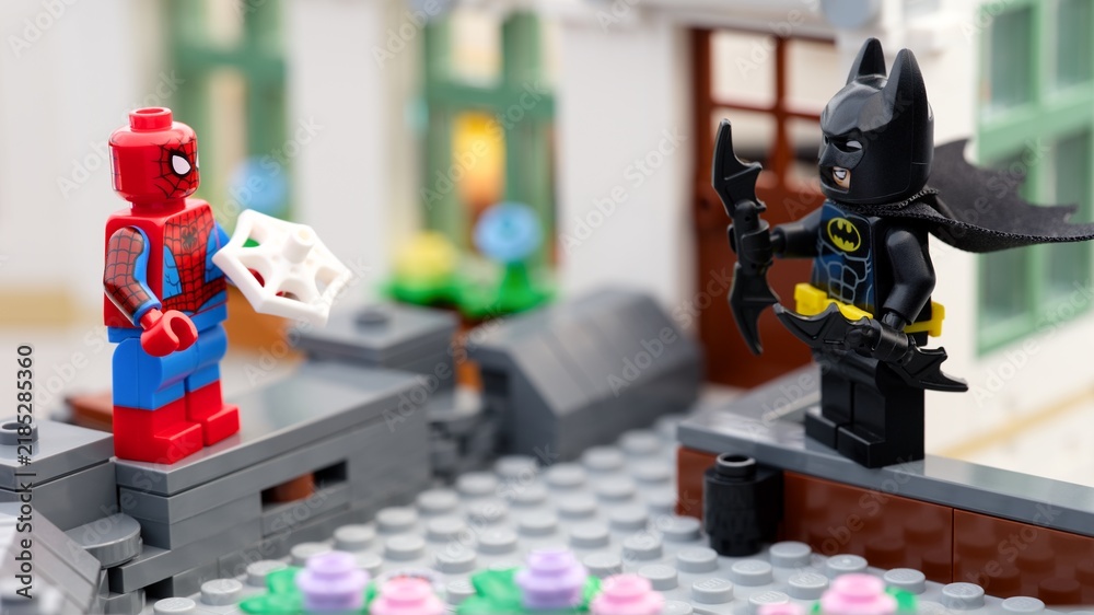 Obraz premium Tambov, Russian Federation - August 23, 2026 A close-up shot of Lego Spider-Man holding a web piece and Batman wielding batarangs while standing opposite each other on a brick rooftop.