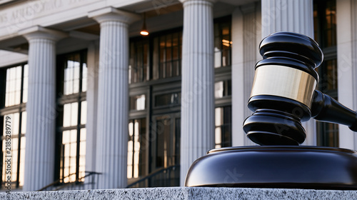 Dark wooden judge gavel against imposing courthouse columns representing legal authority, judicial proceedings, court rulings, justice and the rule of law