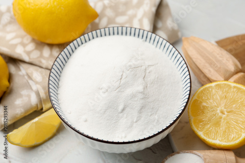 Obraz na płótnie Baking soda in bowl, scoop, lemons and squeezer on white textured table, closeup
