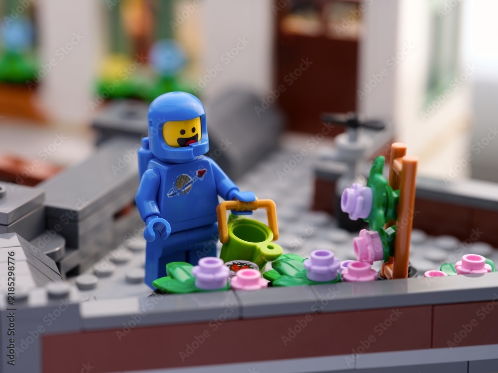 Fototapeta premium Tambov, Russian Federation - September 03, 2026 Blue Lego astronaut minifigure with a watering can next to a flower bed on a rooftop garden.