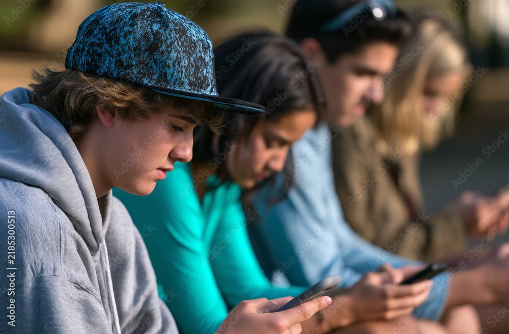 Fototapeta premium Teenagers Sitting on a Bench Using Smartphones in a Park