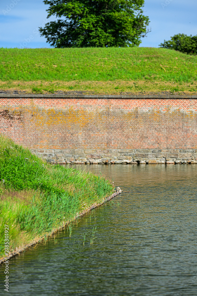 Obraz premium Grassy moat shoreline with historic brick fortification wall.