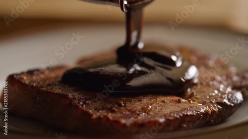 Slow motion close up tracking shot of steak as dark sauce is poured onto seared meat on plate in kitchen