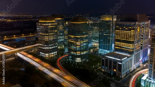 Aerial panning shot of downtown office towers with highway light trails and moving traffic at night