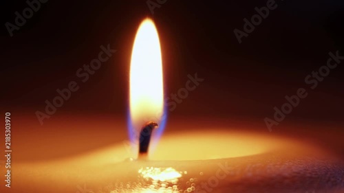 Slow motion static close up of candle flame flickering and wax melting on tabletop in dark indoor setting