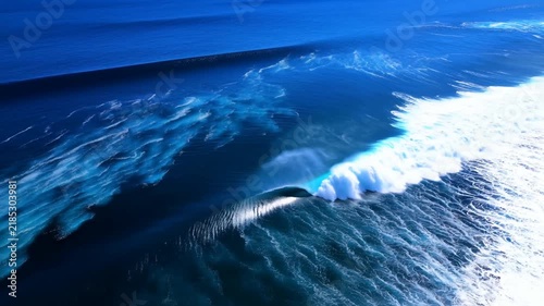 Aerial slow motion tracking pan of ocean waves breaking and curling over reef along open coast from above during daytime