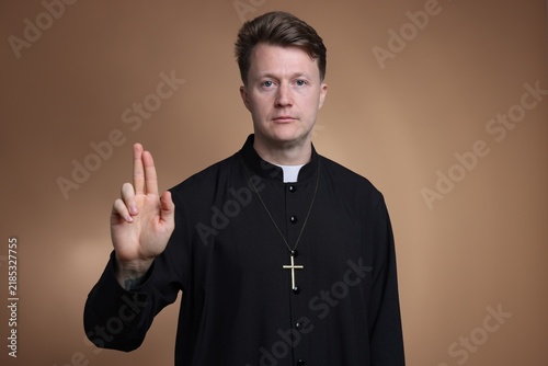 Fotografie Priest in cassock making blessing gesture on pale brown background