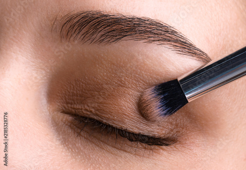 Fototapeta kuchenna Applying nude eye shadow with makeup brush onto woman's face, closeup