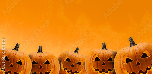 Row of scary carved Halloween pumpkins on orange background with copy space
