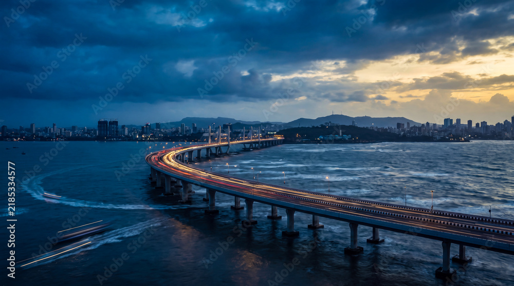 Fototapeta premium Coastal bridge at twilight with city skyline and illuminated traffic lights over ocean