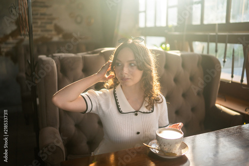 Woman drinking coffee in cafe with warm sunlight and sunglasses