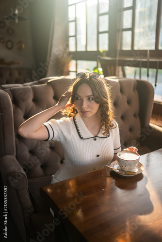 Woman drinking coffee in cafe with warm sunlight and sunglasses