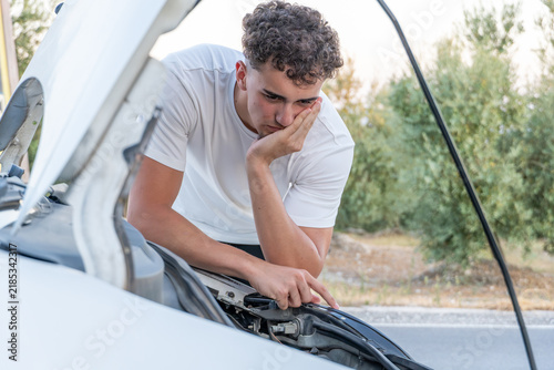 Konstfotografi Frustrated young man looking at his broken down car engine by the side of the ro