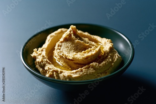 Hummus is placed in a dark green bowl on a matte blue background with soft light