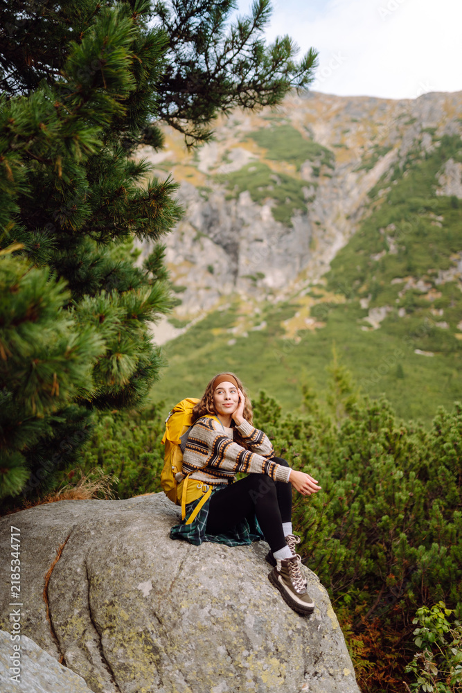 Obraz premium A woman with a hiking backpack enjoys a hike along a rocky mountain trail. The hiker takes in the mountain scenery at sunset. Concepts: adventure, nature, active lifestyle.