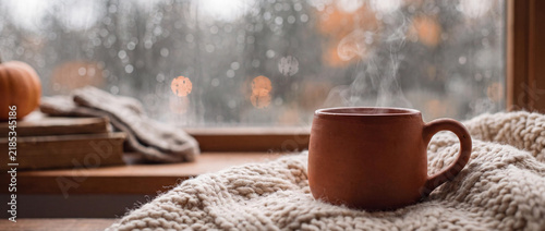 Cozy Autumn Interior Scene with Steaming Ceramic Mug on Knitted Wool Blanket by Rainy Window with Bokeh Lights