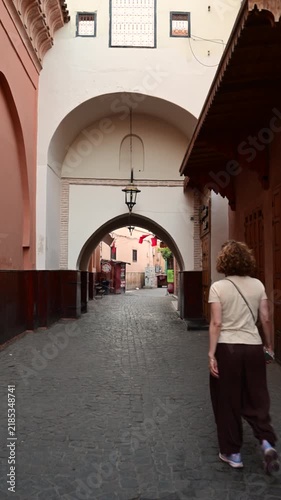 Marrakech, morocco. August 10, 2026. A woman tourist with curly hair wandering through an ancient cobblestone street with arches and traditional moroccan architecture in marrakech