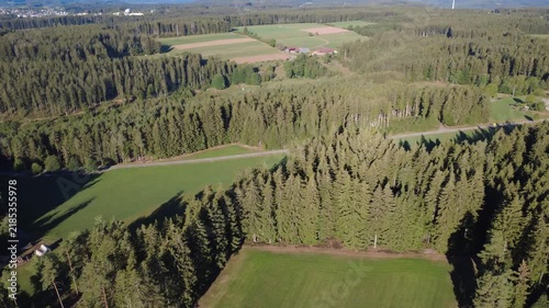 Drone flight over a vast green forest and surrounding rural countryside, with fields and distant landscape stretching toward the horizon on a bright sunny day.