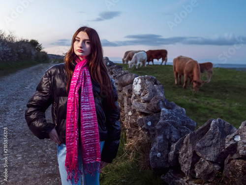 Fotografie Young woman stands beside stone wall, wearing pink scarf and black jacket