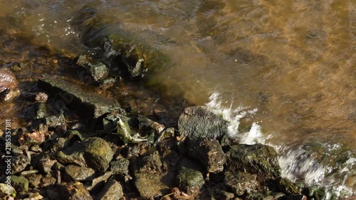 Close view of water movement along rocky shore, showing natural aquatic environment, river landscape and outdoor nature scene