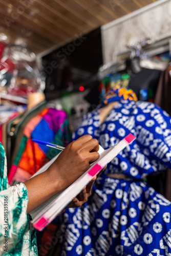 African woman business owner writing inventory in a notebook, managing her small business fashion boutique
