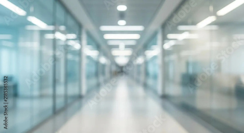 Blurred view of a modern bright office hallway with glass walls and ceiling lights.