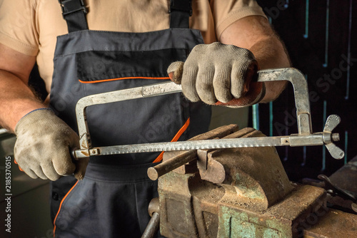 A skilled artisan carefully uses a hacksaw to cut metal, showcasing their focus and craftsmanship. The warm light of dusk enhances the workshop's atmosphere