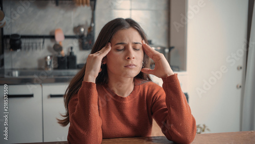Young Latina woman in her home kitchen experiencing a migraine, physical discomfort, and fatigue, highlighting pain, exhaustion, and personal wellness concerns.