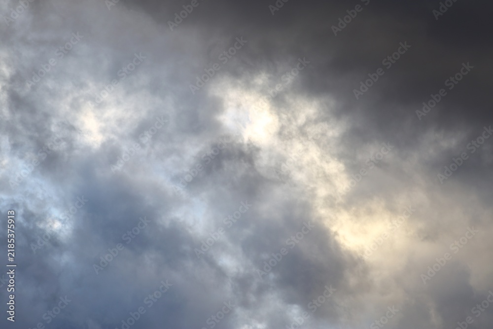 Fototapeta premium Sunlight breaking through dark storm clouds in dramatic grey sky background