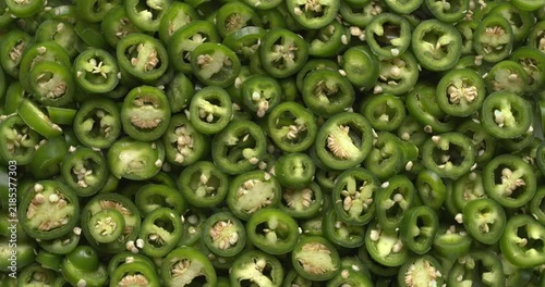 Sliced jalapeño peppers full-frame background texture. Fresh green chili rings for homemade spicy pickles, slowly rotating in a top view with backlit natural window light.