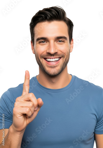 young handsome caucasian man in a steel blue t-shirt, smiling broadly and pointing one finger up on a clean high-key white studio background, concept of success and achievement