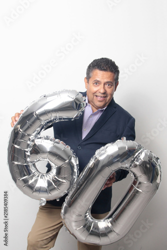 60-year-old Latino man with a dark skin displays 60 shaped balloons to celebrate his birthday and his entry into his old age