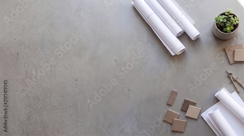 Flat lay of an architect workspace on a concrete desk with rolled blueprints and brown ceramic tiles, construction project planning, professional architectural background with left copy space