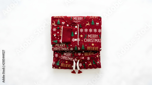 Folded red Christmas pajamas featuring a festive pattern of trees and text lie flat on transparent background.