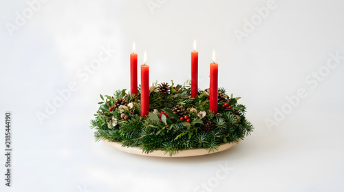 Advent wreath decorated with red candles and green fir branches sits on a transparent surface.